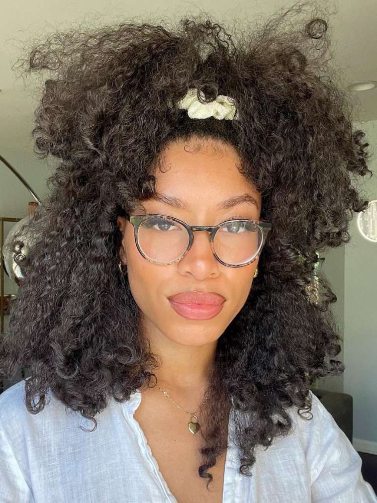 Mulher de pele negra usando óculos de grau e cabelo cacheado preso com scrunchie