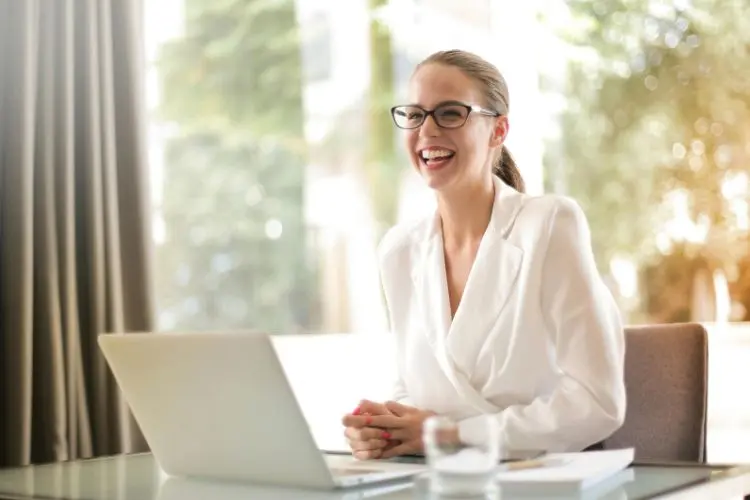 Foto de mulher de negócios sentada em frente a um notebook. Ela usa óculos, cabelos presos e uma camisa branca