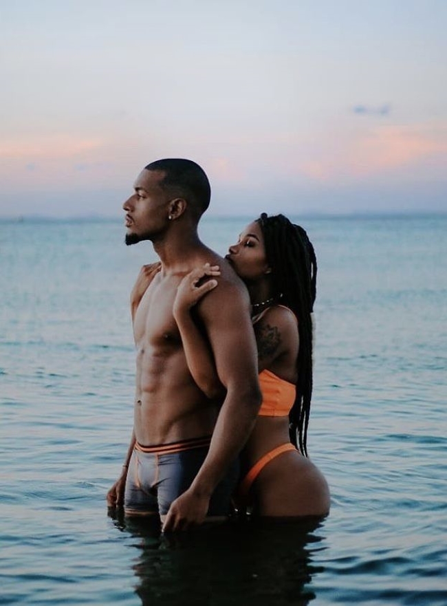 Homem e mulher de pele negra abraçados no mar 