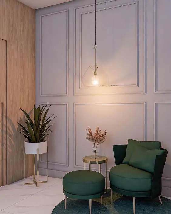 Hall com parede cinza com moldura boiserie, vasos e poltrona com puff em verde