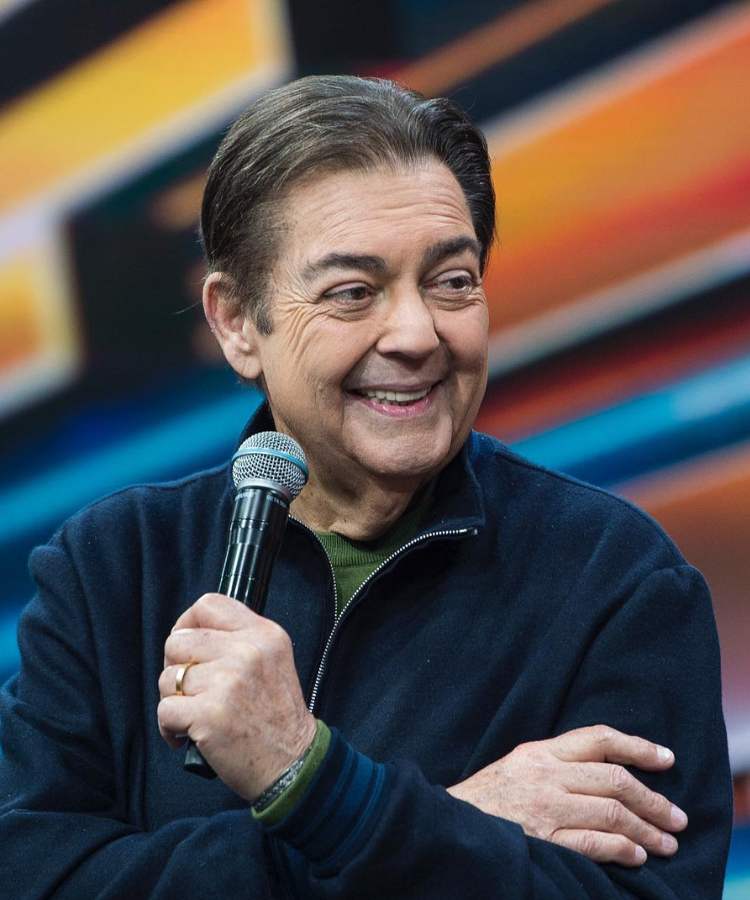 Apresentador Faustão no seu programa na Band, segurando microfone e sorrindo