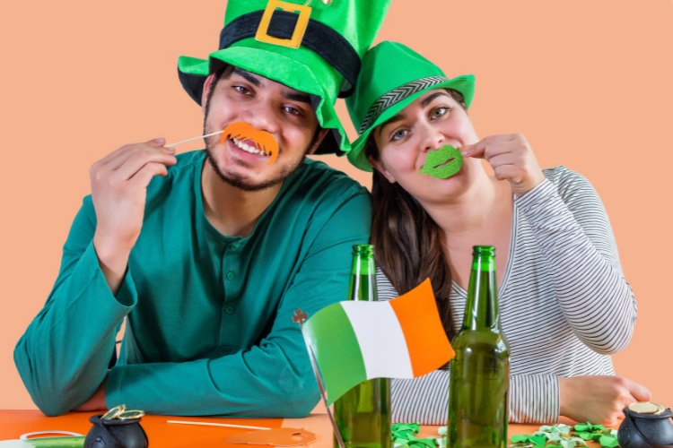 Homem e mulher sentados à mesa com chapéu de duende, decorações da Irlanda e cerveja 