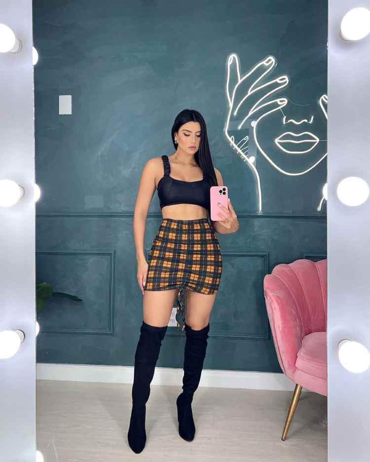 mulher com top preto e saia xadrez amarela