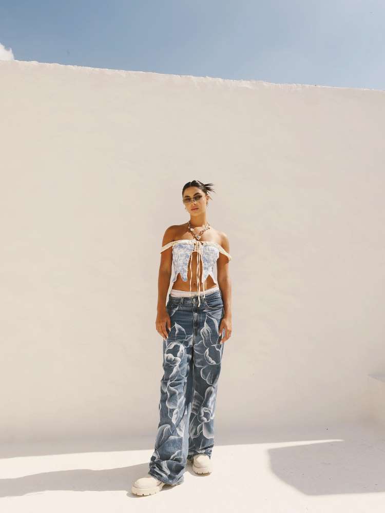 Gabi Versiane em fundo branco usando cropped branco amarrado e calça jeans larga com desenhos de flores em branco