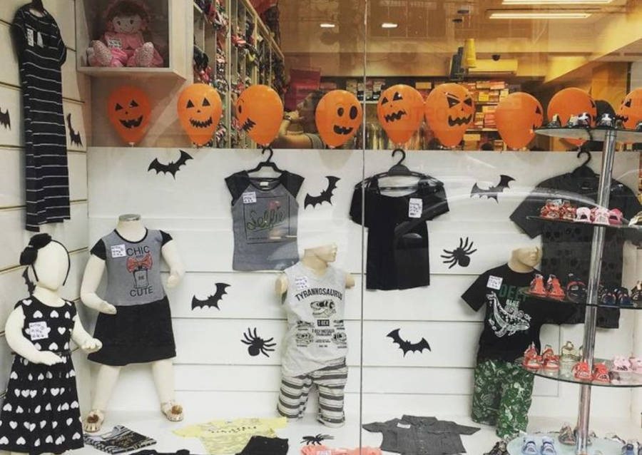 Foto de vitrine infantil enfeitada para o Halloween, com bexigas de abóbora e desenhos de morcego 