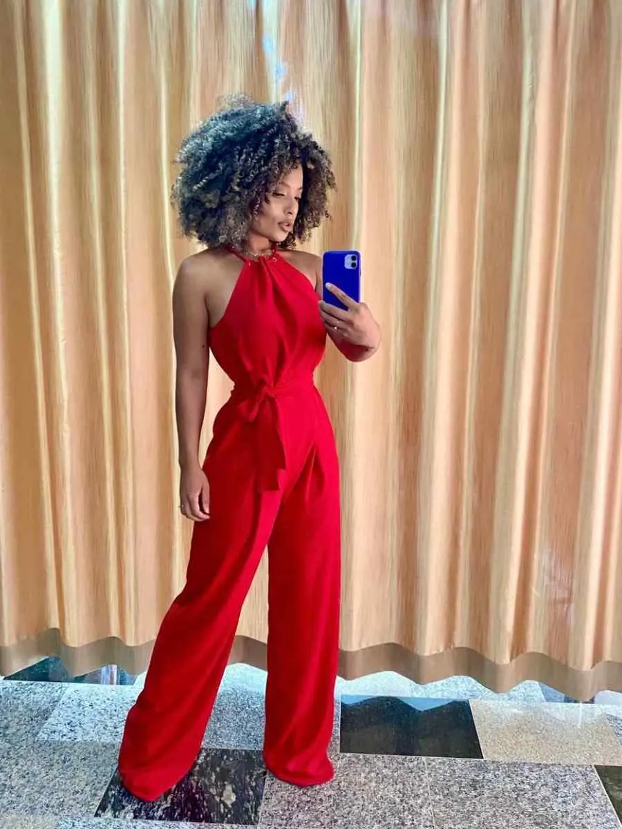 Mulher de pele negra usando look vermelho para o Natal composto por macacão com amarração no pescoço