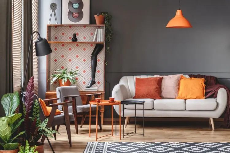 Sala com móvel com papel de parede laranja, sofá pé de palito com almofadas laranjas, tapete estampado, quadro de dico de vinil e luminária laranja