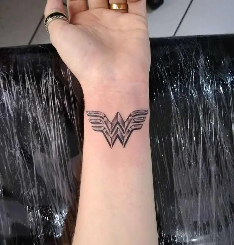 tatuagem sombreada de símbolo mulher maravilha no pulso de pessoa de pele clara