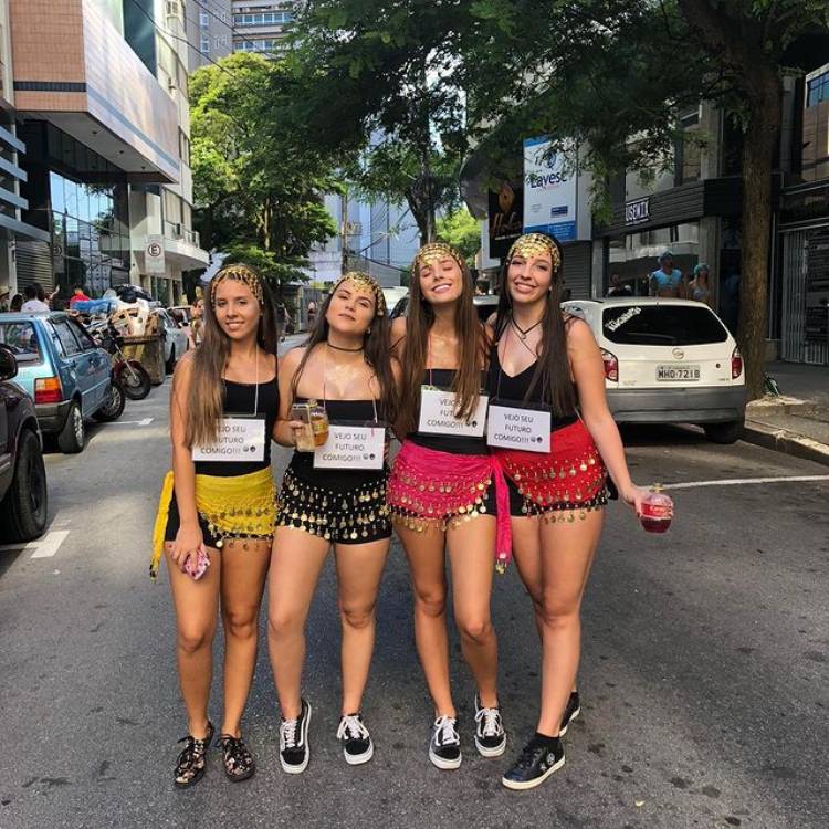 Amigas na rua fantasiadas de videntes com a plaquinha "vejo seu futuro comigo"