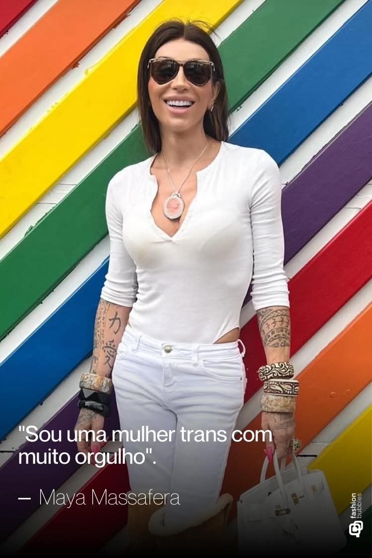 Uma mulher trans sorridente, com óculos escuros e cabelo castanho, usa uma roupa branca ajustada, com tatuagens nos braços e pulseiras. Ela está em frente a uma bandeira de arco-íris, com uma citação de Maya Massafera.
