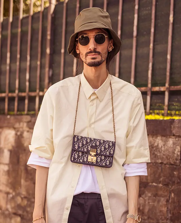Homem usa camisa, bucket hat e bolsa pendurada no pescoço