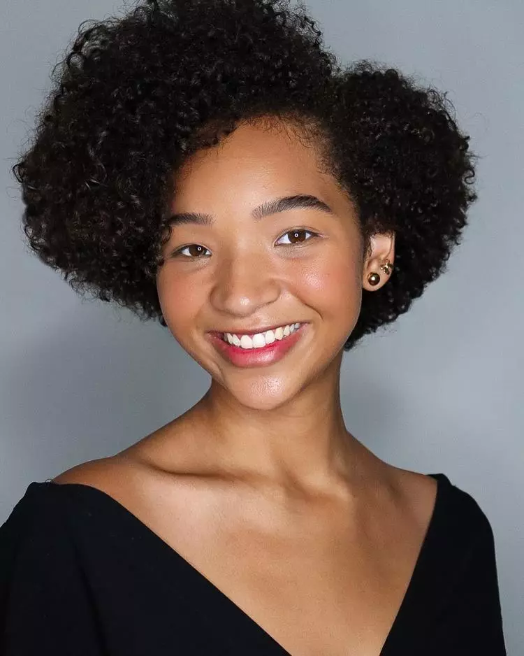 Mulher negra com cabelo crespo, make leve, usando brincos dourado e roupa preta