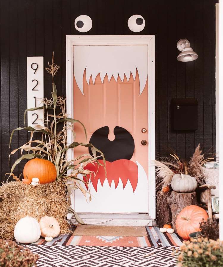 Decoração de entrada com parede marrom, porta rosada imitando boca de monstro, feno e abóboras