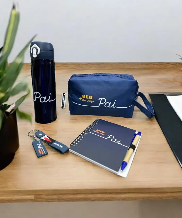 Conjunto de itens personalizados com a palavra “Pai”, incluindo garrafa, estojo, chaveiro, caderno e caneta sobre uma mesa.