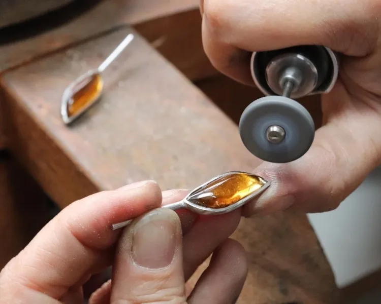 Joalheiro fazendo brincos com metal prateado e pedra amarelada