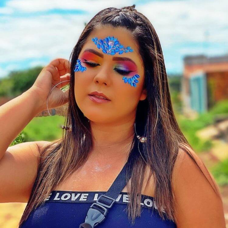 Mulher de pele clara com sombra colorida e pedrarias azuis na testa e abaixo dos olhos