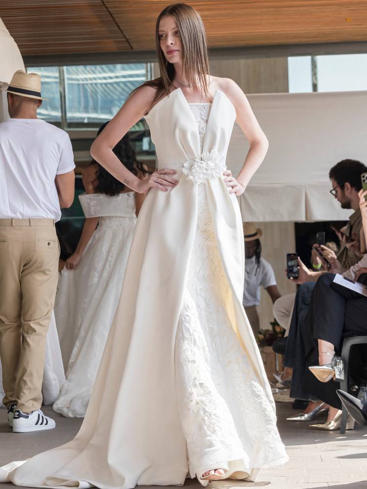 Mulher de pele clara desfilando com vestido de noiva com recortes, flores e rendas