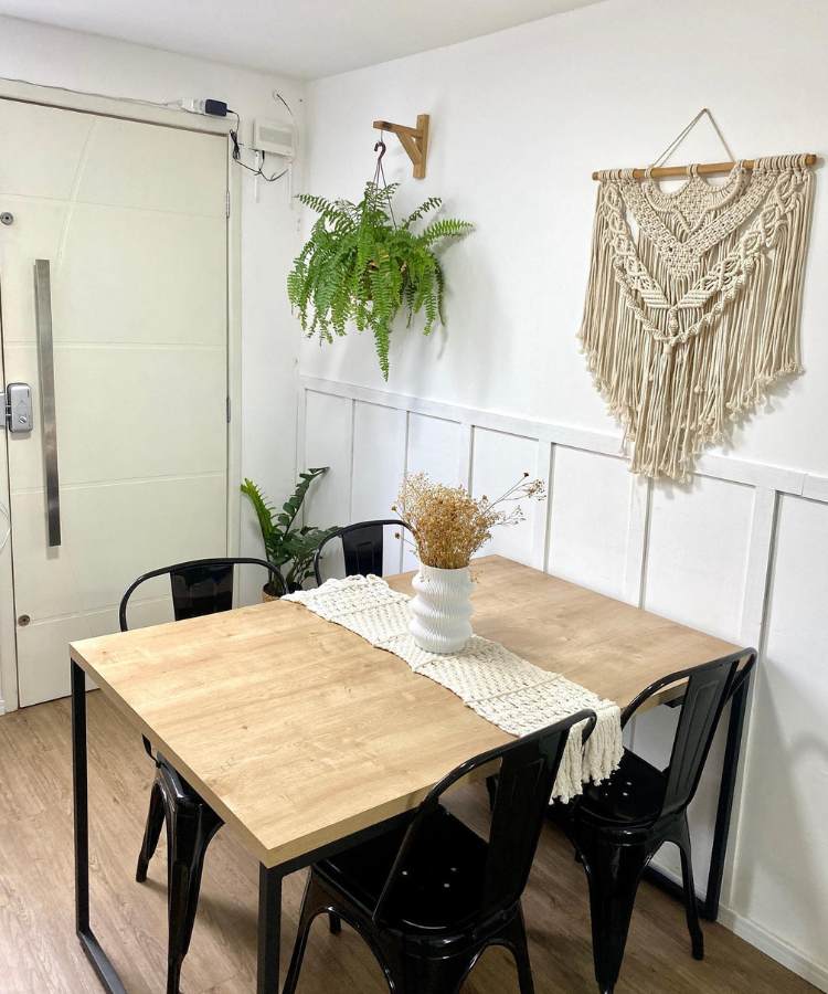 Sala de jantar com mesa e cadeiras pretas, na parede uma samambaia pendurada e uma zamioculca no canto