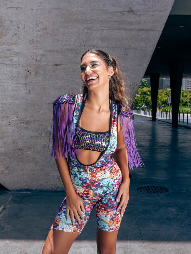 Mulher de pele clara com top furtacor, macaquinho colorido  e ombreira de franjas roxas 