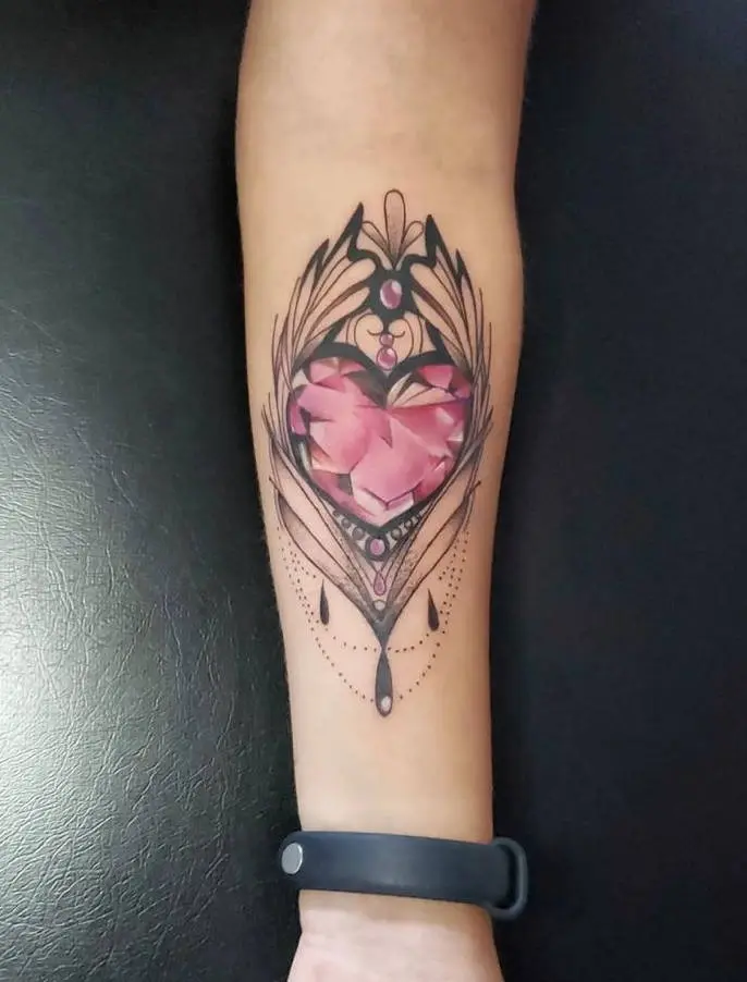 Tatuagem de coração rosa imitando pedra e arabescos em volta no antebraço