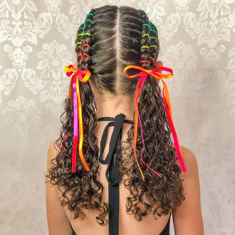 Cabelo escuro cacheado com duas tranças e com fitas e elásticos coloridos.