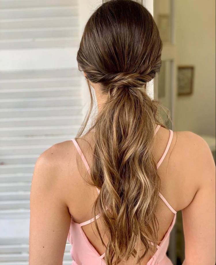 Mulher de pele clara com cabelo moreno iluminado em rabo de cavalo com torcido