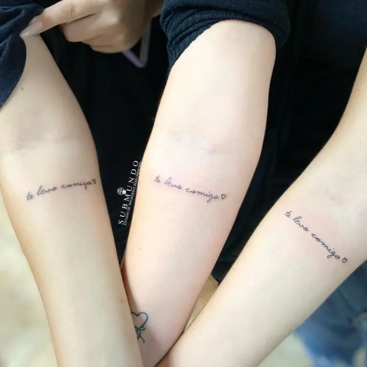 Tatuagem de mãe e filhas com a frase Te levo comigo em letra cursiva