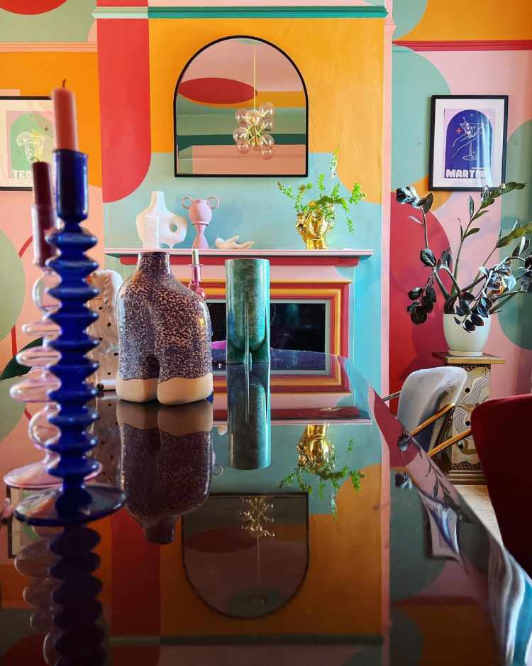 Sala com parede colorida, mesa preta, plantas e itens decorativos coloridos