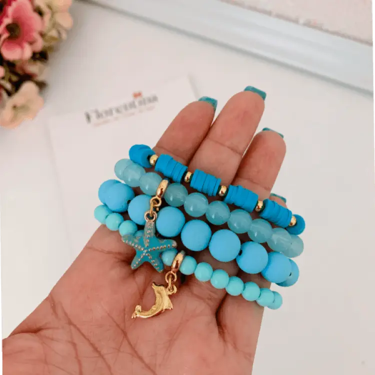 Mão de pele clara segurando pulseiras azuis com temas marinhos