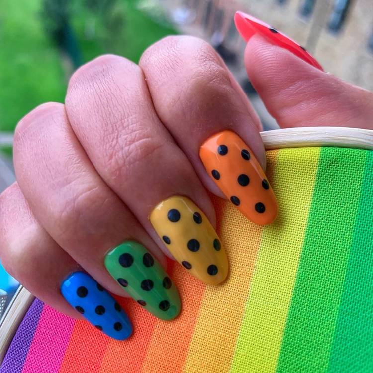Mão com unhas arco-íris LGBTQIA+:  Polegar: Indicador: vermelho com bolinha preta Médio: laranja com bolinha preta amarelo com bolinha preta Anelar: verde com bolinha preta Mínimo azul com bolinha preta