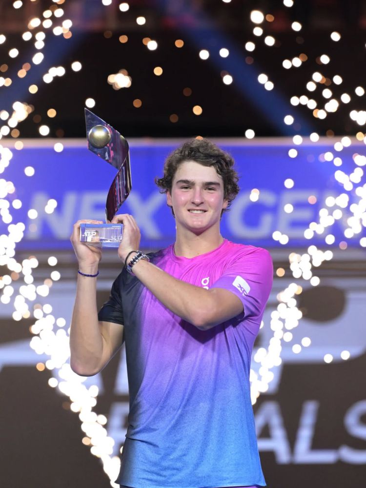 João usando blusa degradê rosa e azul segurando troféu do Next Gen ATP Finals