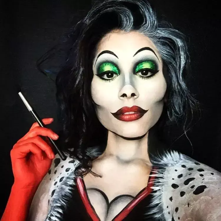 Pessoa usando maquiagem de Cruella, com sombra verde, cabelo branco e preto, luvas de tinta vermelha e roupa de dálmata