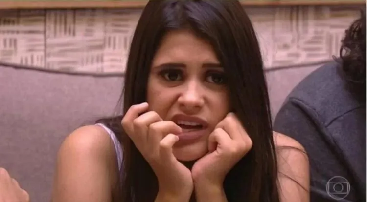 Ana Paula sentada usando regata branca e comendo unha