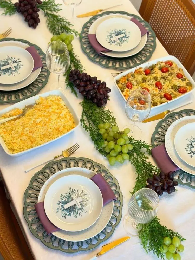 Mesa posta com sousplat cinza, prato com cruz e travessas com bacalhau 