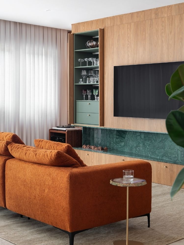 Sala de TV com painel de madeira, cristaleira, sofá terracota 