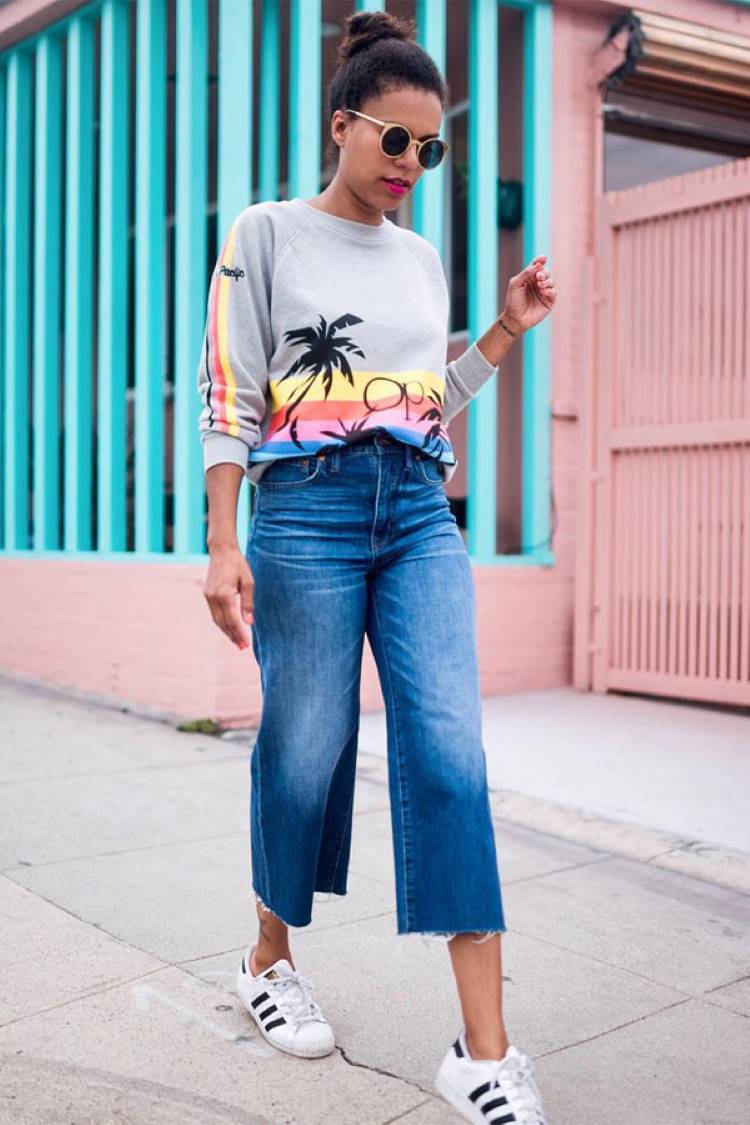 Mulher de pele morena usando moletom cinza com paisagem, calça pantacourt e tênis Adidas