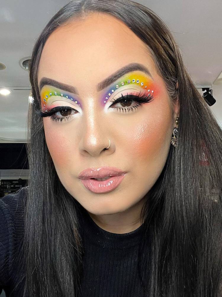 Mulher de pele clara e cabelo preto com sobra colorida, delineado e strass prata. 
