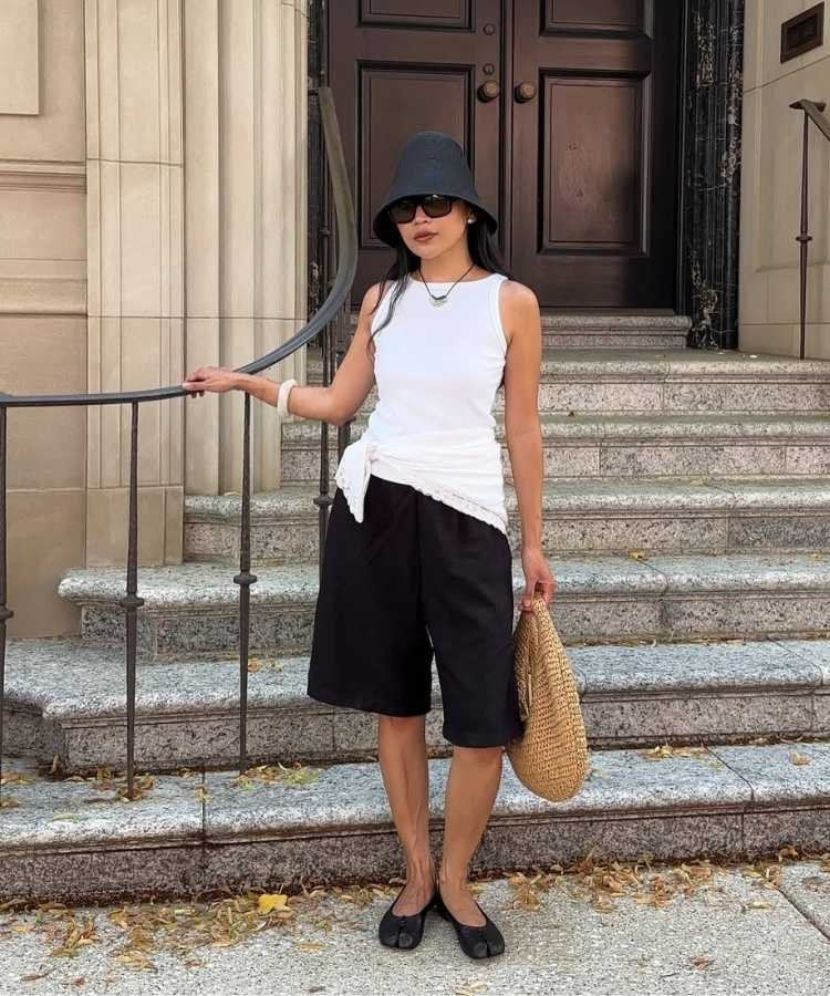 Foto de mulher morena usando regata branca com bermuda de alfaiataria preta, um dos looks para trabalhar no calor