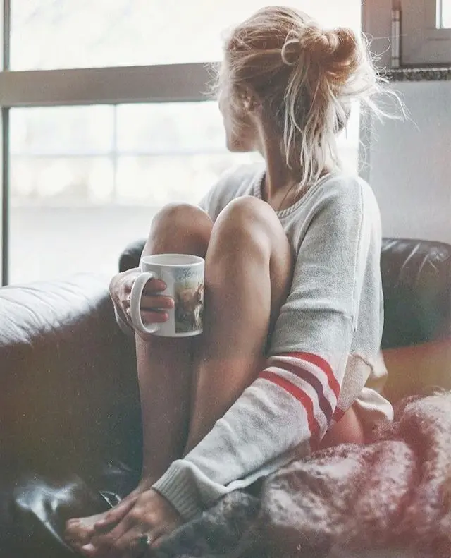 Frase para foto pensativa mulher loira com coque, toma café e usa moletom cinza