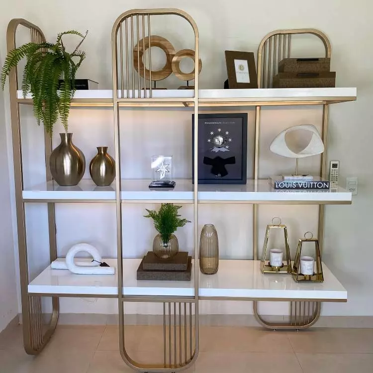 Estante vazada com vasos de planta, quadro, porta-retrato e diversos itens decorativos. 