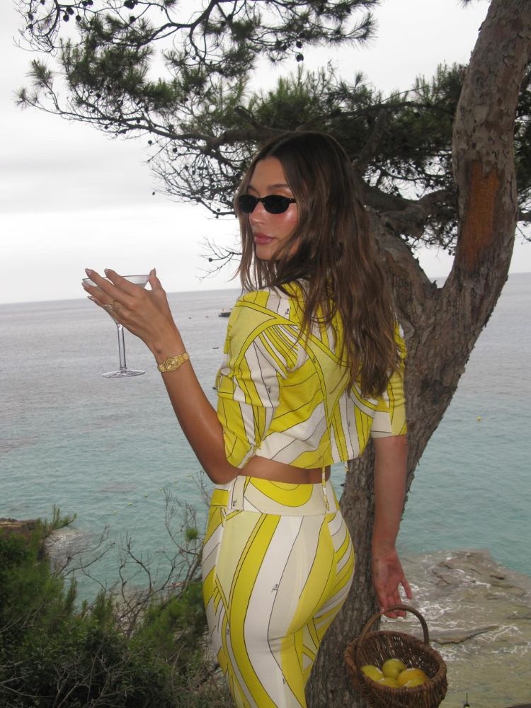 Hailey Bieber usando conjunto de blusa e saia branco e amarelo e micro óculos de sol