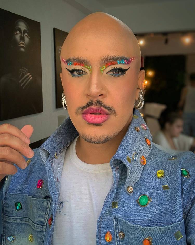 Homem com maquiagem para o Carnaval, com delineado, sombra colorida com pedrinhas e batom