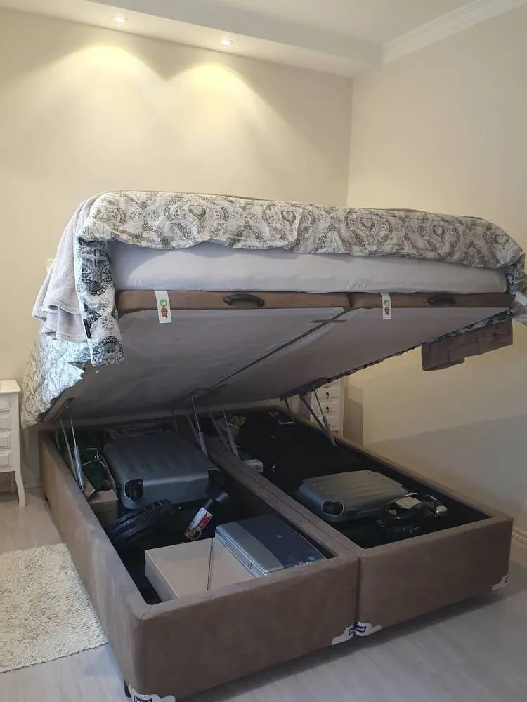 Cama-baú com roupa de cama cinza e diversas malas no baú. 