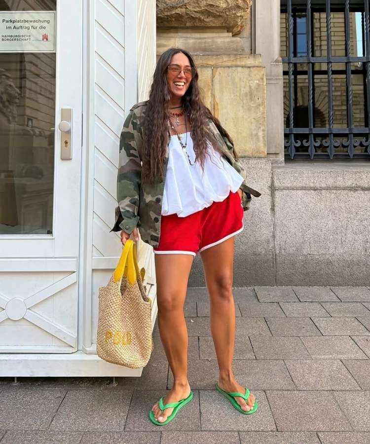 Mulher usando jaquets com estampa camuflada, bata branca e shorts esportivo vermelho