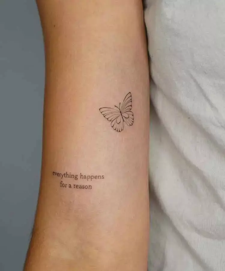 A imagem mostra uma tatuagem minimalista no braço, composta pela frase em inglês "everything happens for a reason" e um desenho delicado de uma borboleta acima. A tatuagem é discreta, com linhas finas, destacando-se sobre a pele clara.