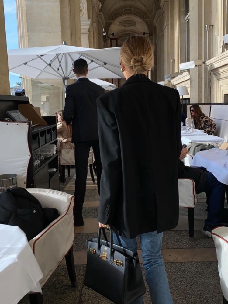 mulher usando blazer preto com calça jeans bolsa preta e cabelo preso