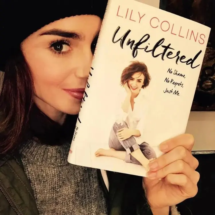 Lily Collins com roupas de frio segurando seu livro 