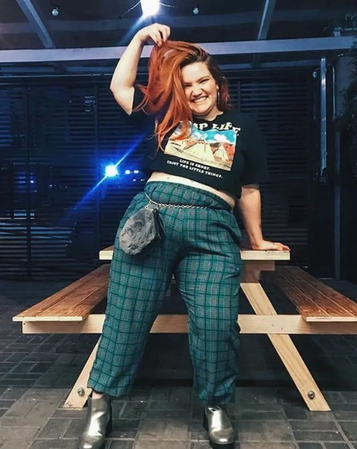 Moça sorrindo de calça xadrez verde e camiseta cropped estampada
