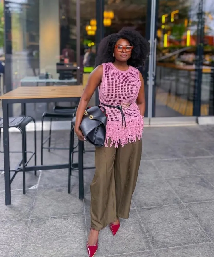 Foto de mulher negra usando regata rosa de crochê e calça de alfaiataria marrom, um dos looks para trabalhar no calor