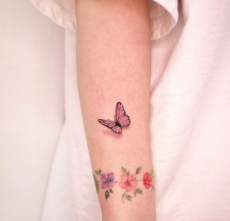 braço de pele clara com tatuagem de borboleta colorida e bracelete de flores coloridas